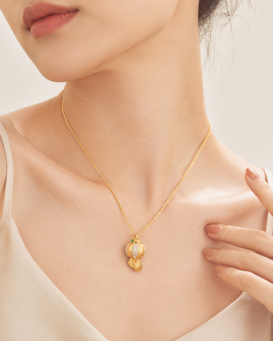 CARV. gold pumpkin pendant necklace with green stone accent worn at collarbone close-up