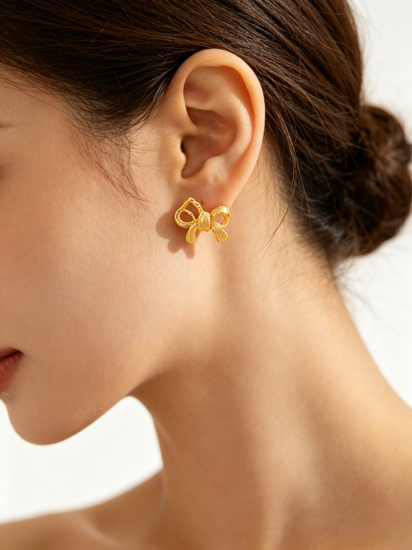 CARV. gold bow stud earrings worn on ear with sculptural ribbon shape and pavé detail