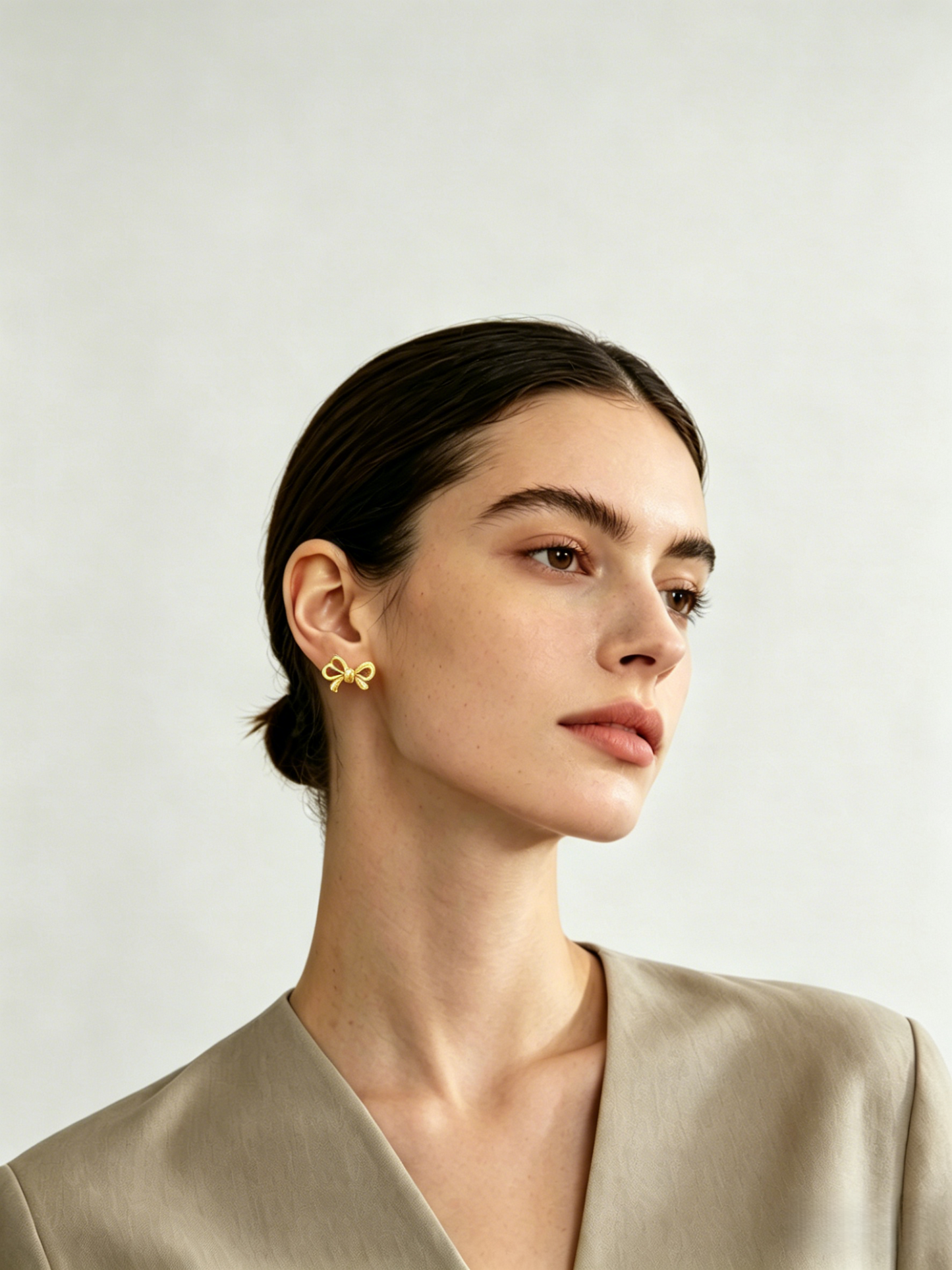 CARV. gold bow stud earrings shown on ear in portrait view with polished ribbon design