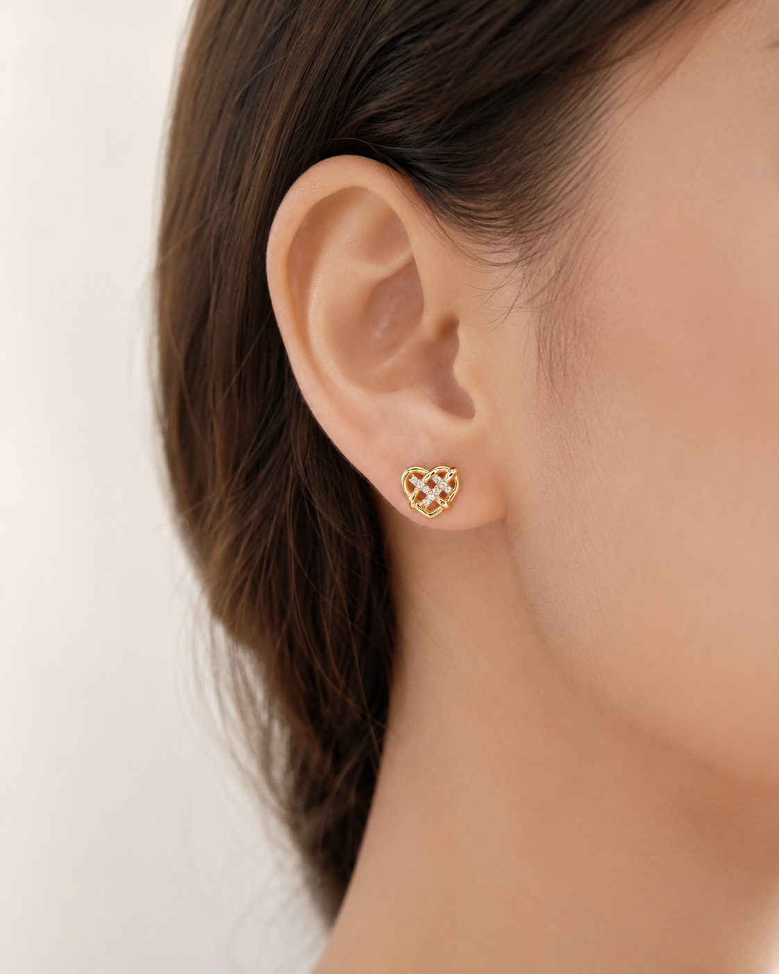 CARV. gold heart stud earrings with crystal knot detail worn on ear close-up