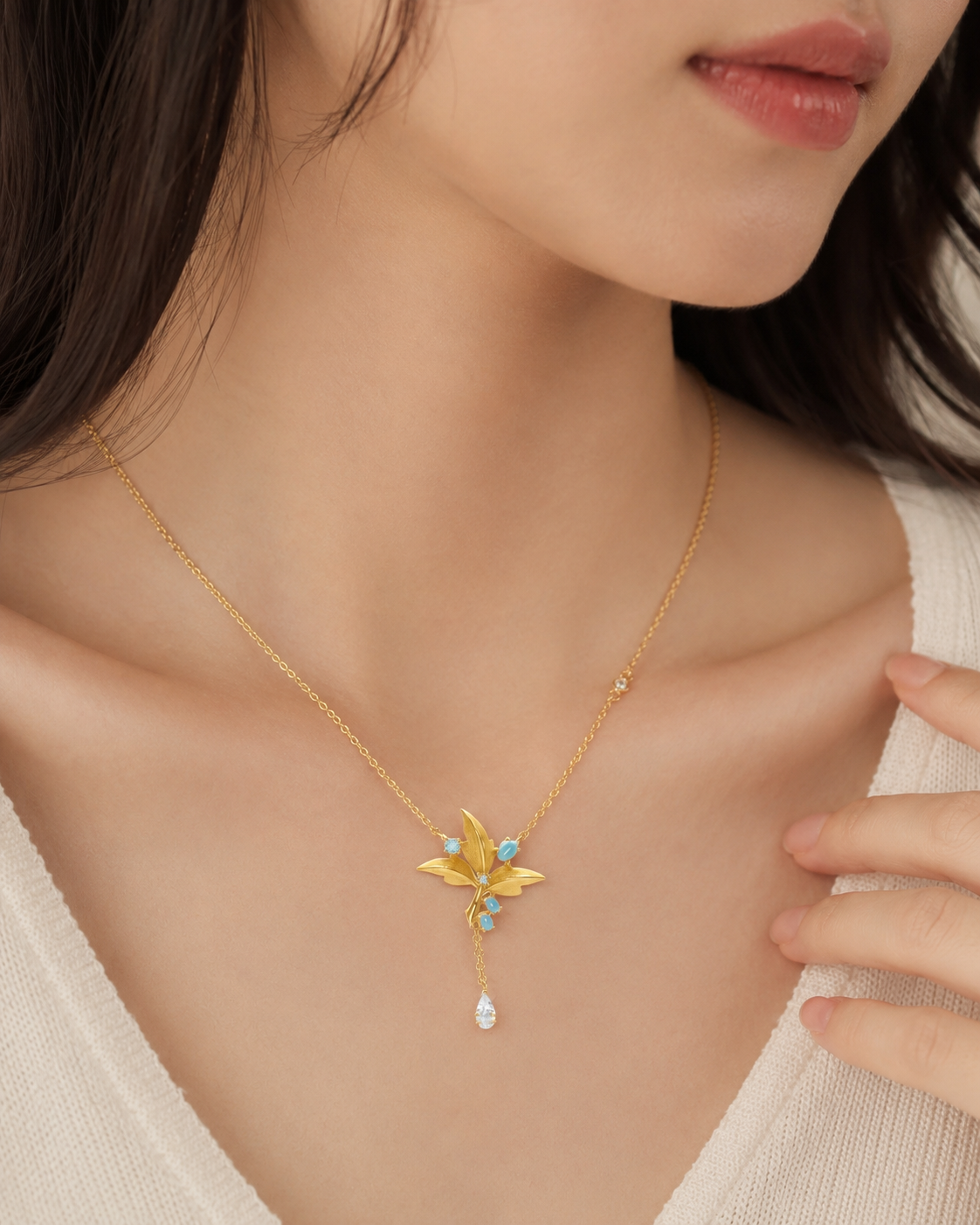 CARV. gold lily pendant necklace with turquoise accent worn at collarbone in close-up view