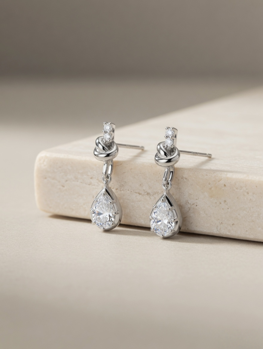 CARV. silver bow knot drop earrings with pear-cut clear stones displayed on a stone surface